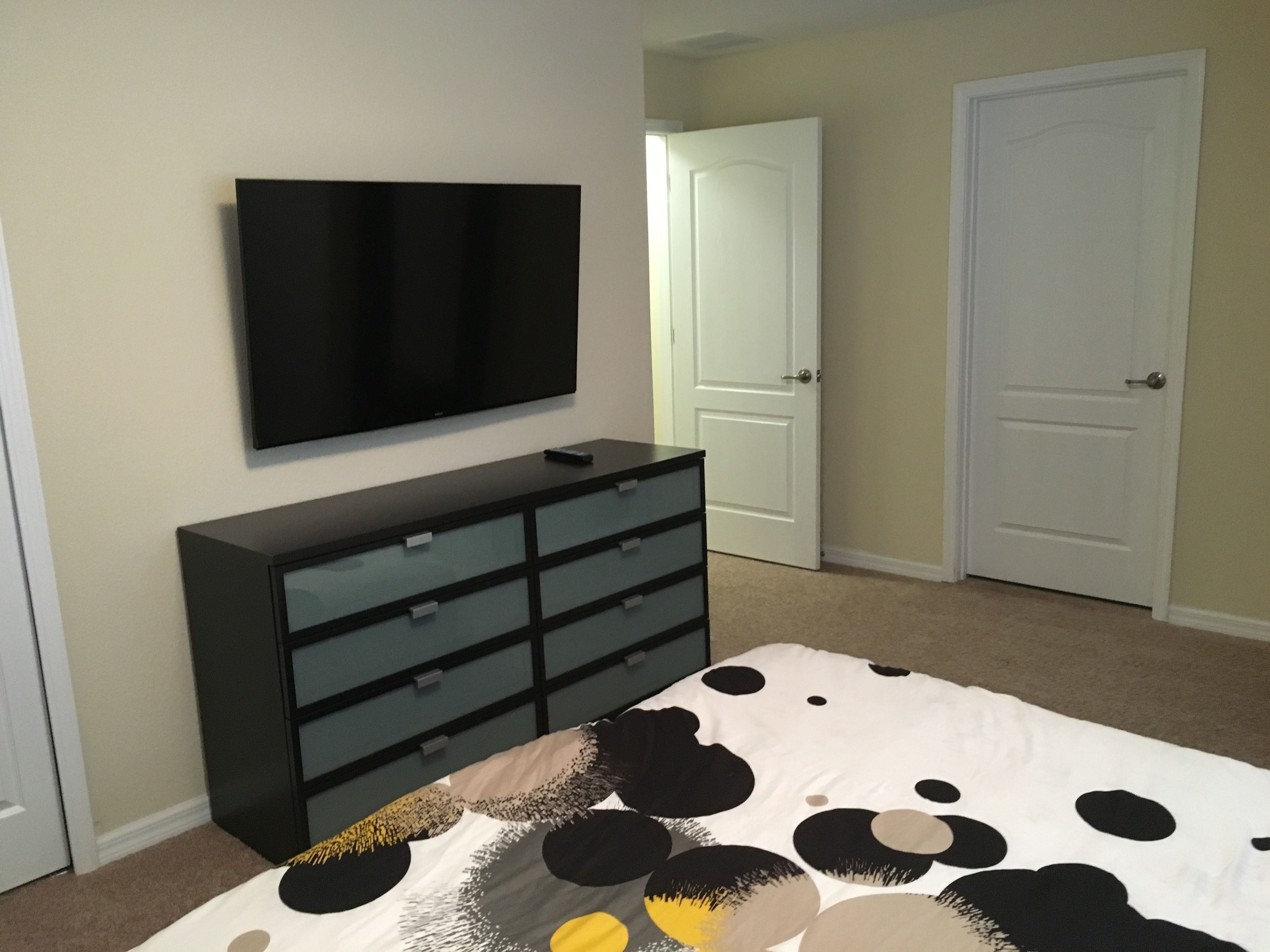 A bedroom with a bed, a dresser, a television mounted on the wall, and two doors.