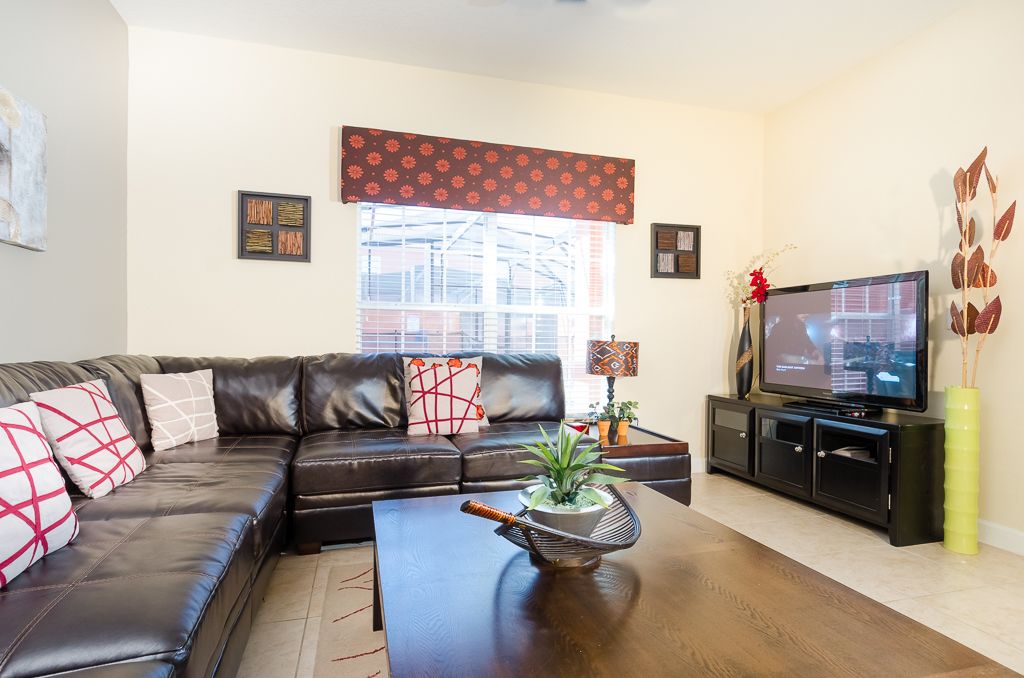 A modern living room with a leather sofa, a coffee table with a plant, a television on a black stand, and a window with a patterned valance.