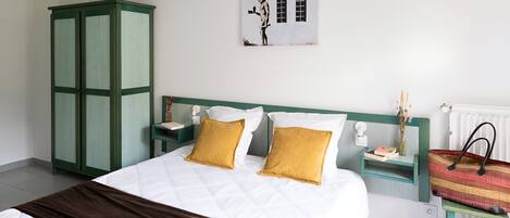 Un dormitorio con una cama, un armario verde, mesitas de noche, una obra de arte colgada en la pared y un radiador.
