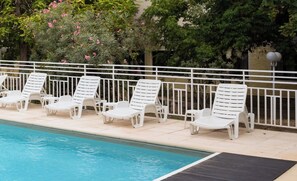 A poolside area with white lounge chairs and a white fence.