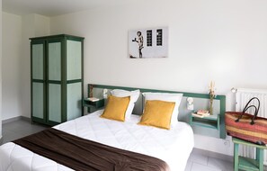 A bedroom with a bed, a green wardrobe, a nightstand with a lamp, a framed picture on the wall, and a radiator. - Appart Hôtel Corte HR (Corte)