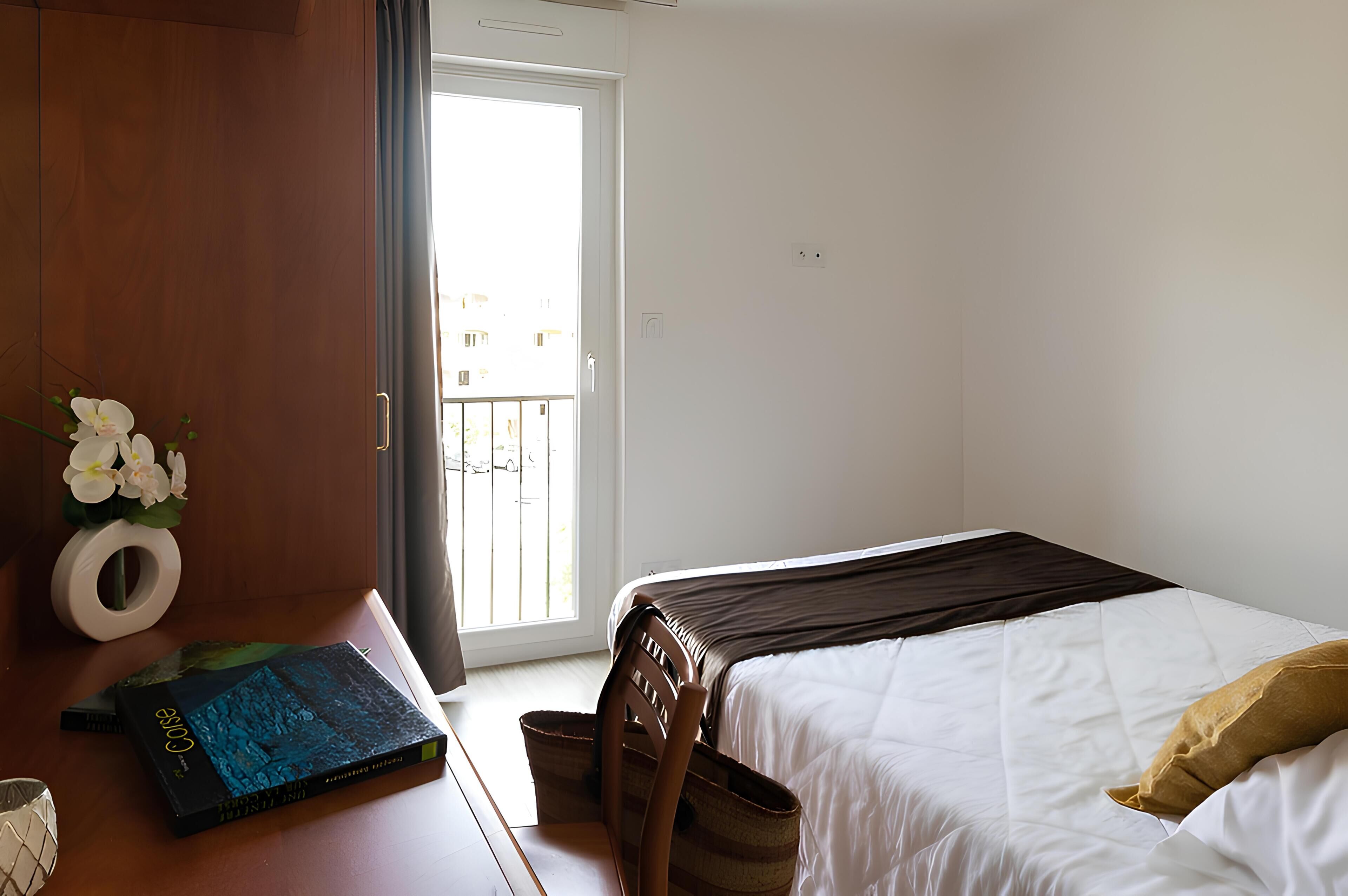 Una camera da letto con un letto, una scrivania con un libro, una sedia e una finestra vista.