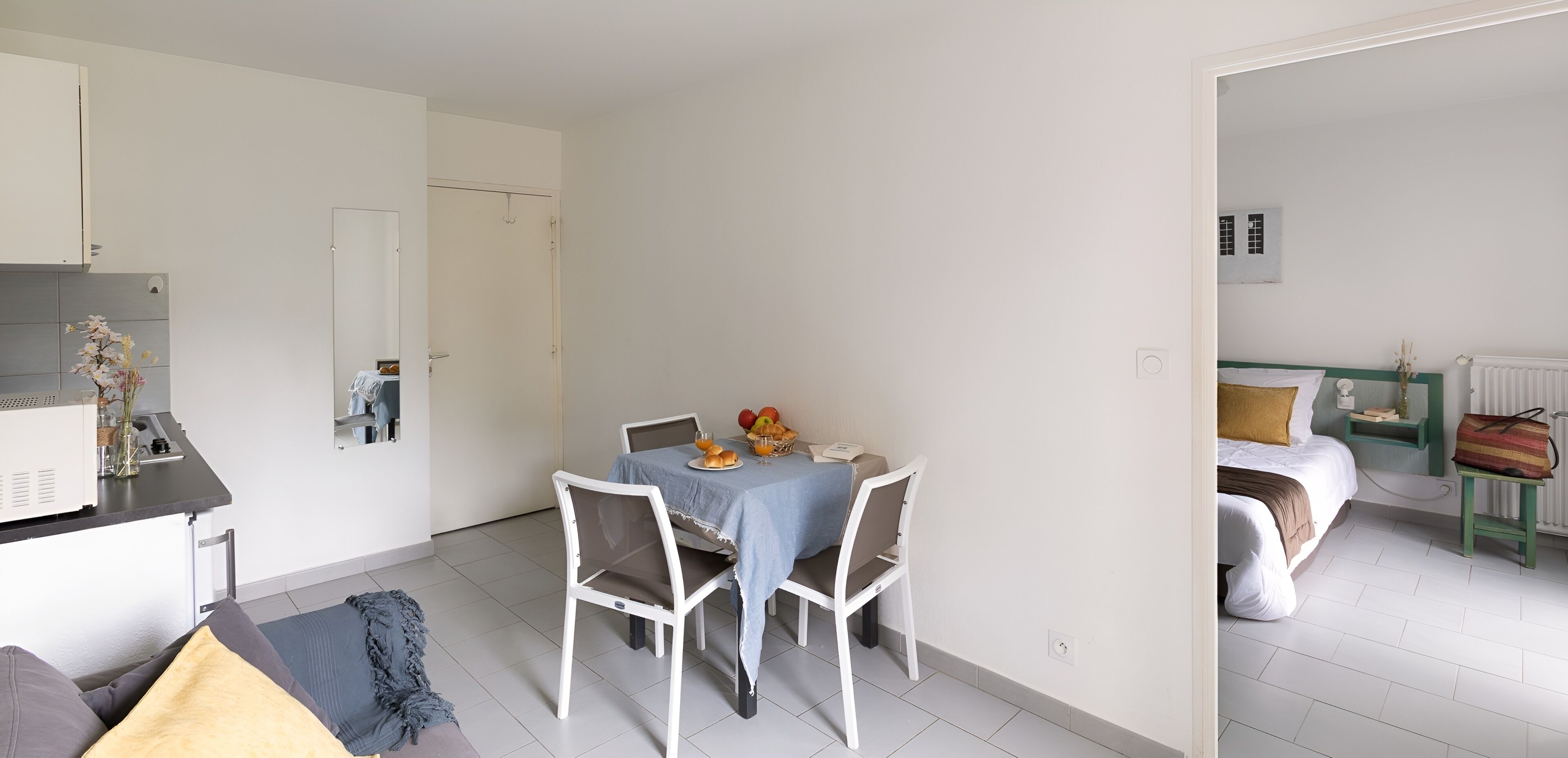 Un espacio habitable compacto con comedor, kitchenette y un dormitorio con cama y mesita de noche.