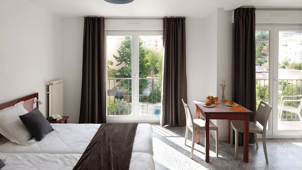 A hotel room with a bed, a table with breakfast, a chair, and a view of the outside. - Appart Hôtel Corte HR (Corte)