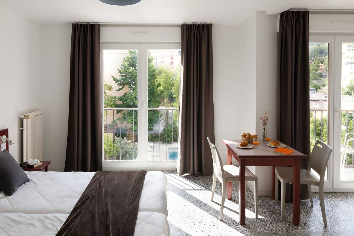 Habitación de hotel con cama, una mesa con desayuno, una silla y vistas al exterior.
