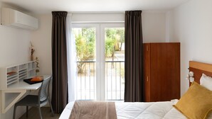 A hotel room with a bed, a desk, a wardrobe, and a balcony with curtains. - Appart Hôtel Corte HR (Corte)