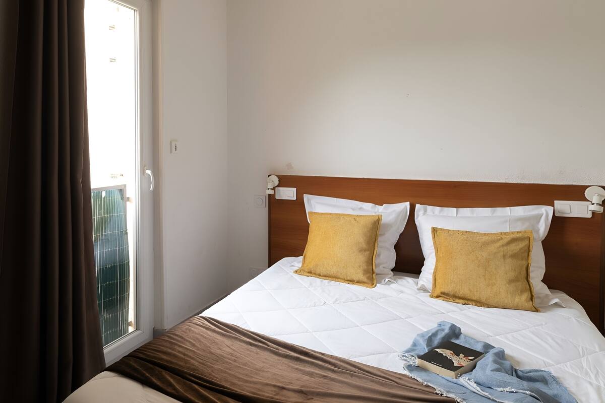 Una habitación de hotel con cama, dos almohadas, una colcha y un libro.