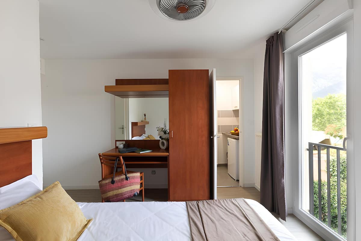 Habitación de hotel con cama, escritorio, silla, espejo y vistas al exterior.