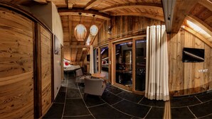 Un intérieur en bois avec un plafond incurvé, un sol en pierre, un coin repas avec des chaises, un lit et un téléviseur.