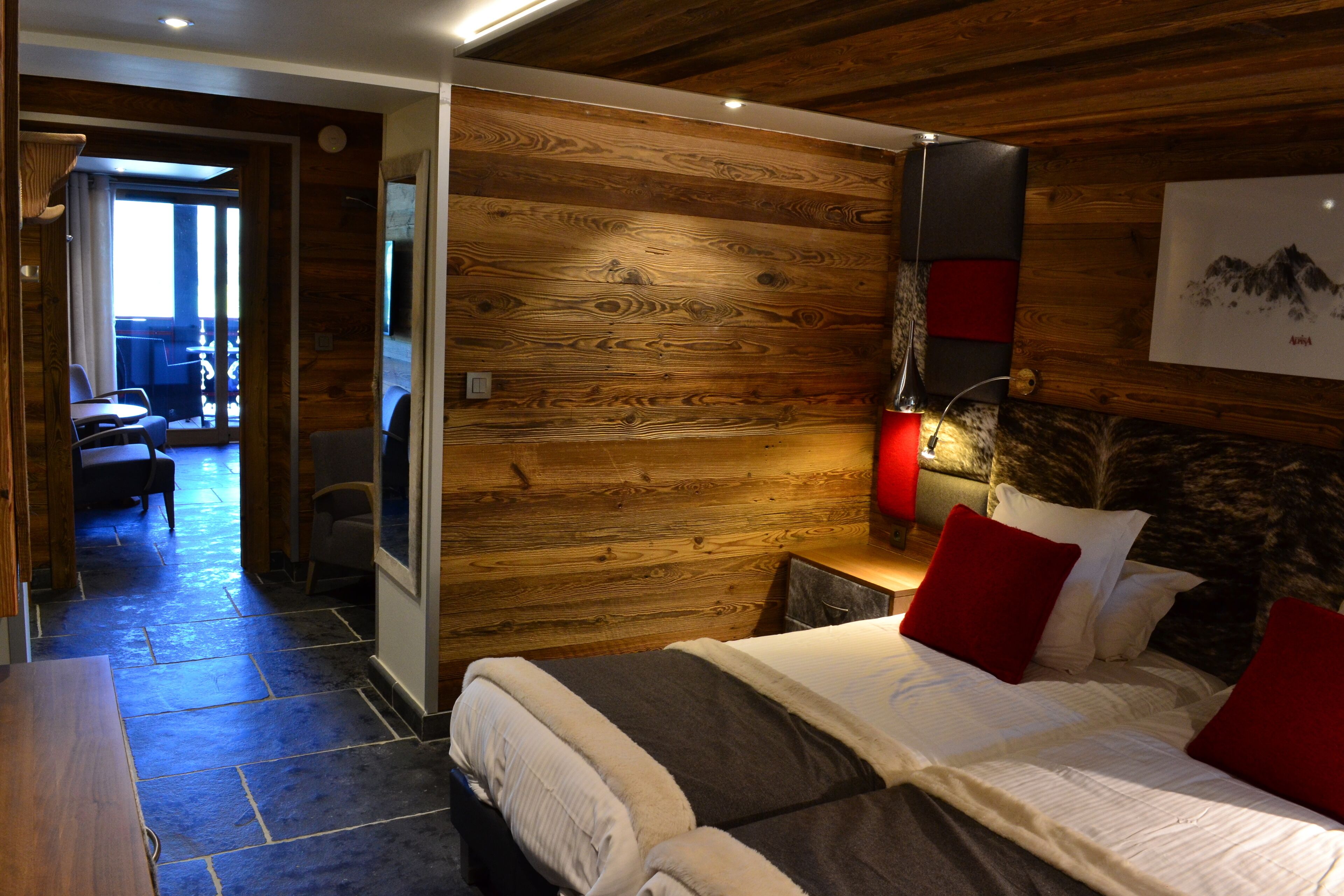 Une chambre avec un mur en bois, un lit avec des oreillers rouges et blancs, une table de chevet et une lampe.