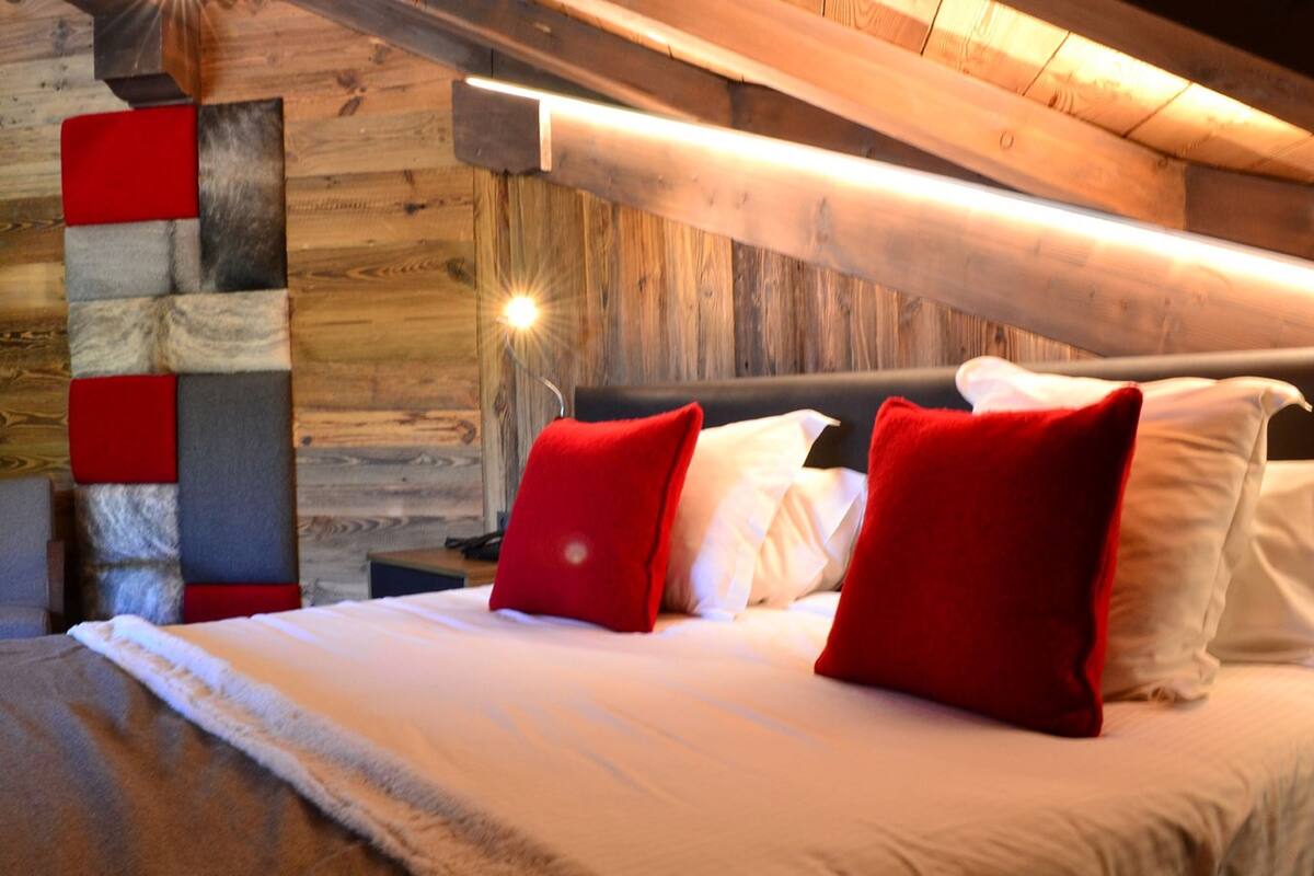 Ein Schlafzimmer mit einem hölzernen Kopfteil, einem Bett mit weißer und roter Bettwäsche und einem modernen Wanddesign.