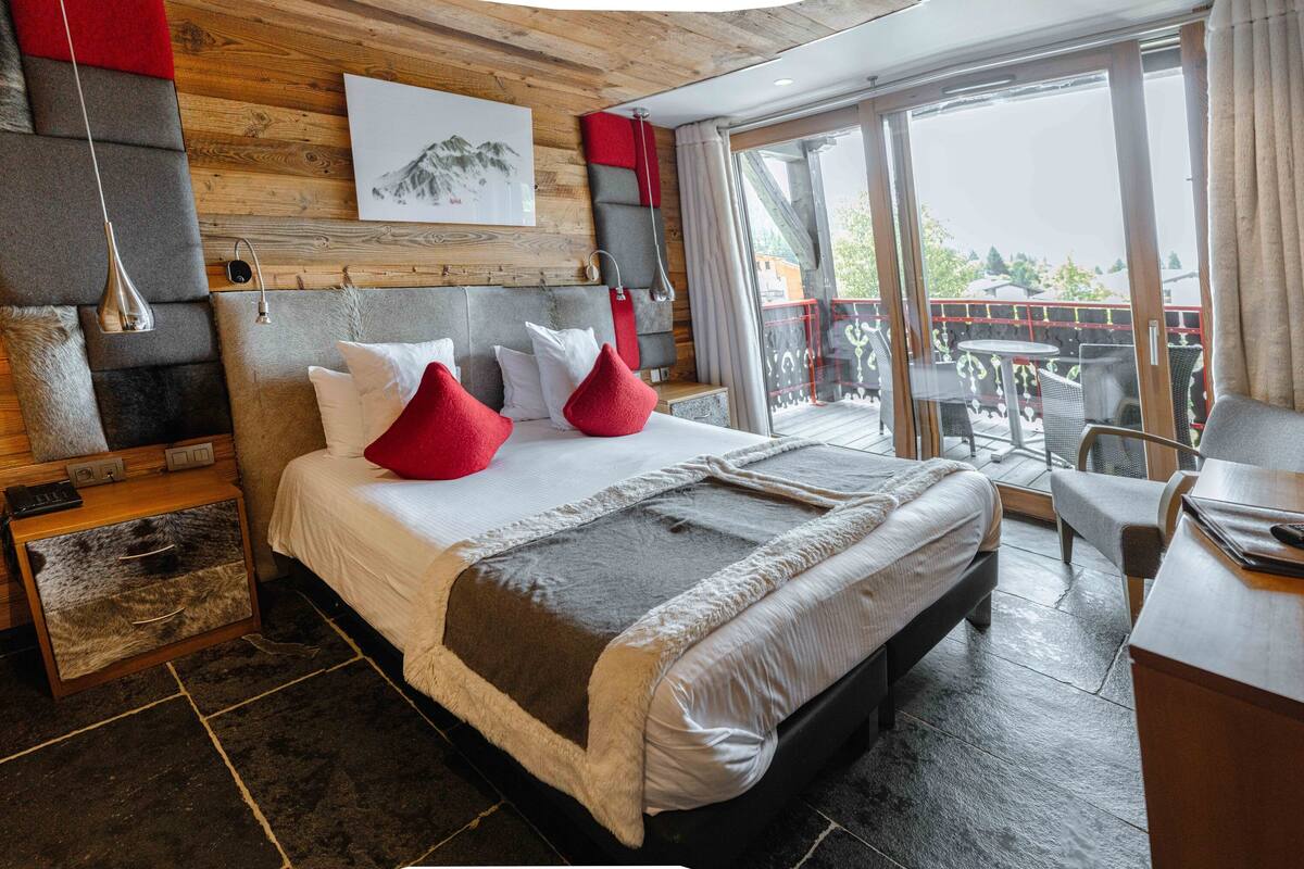 Ein modernes Hotelzimmer mit einem großen Bett, einem Schreibtisch und einem Balkon mit Sitzgelegenheit.