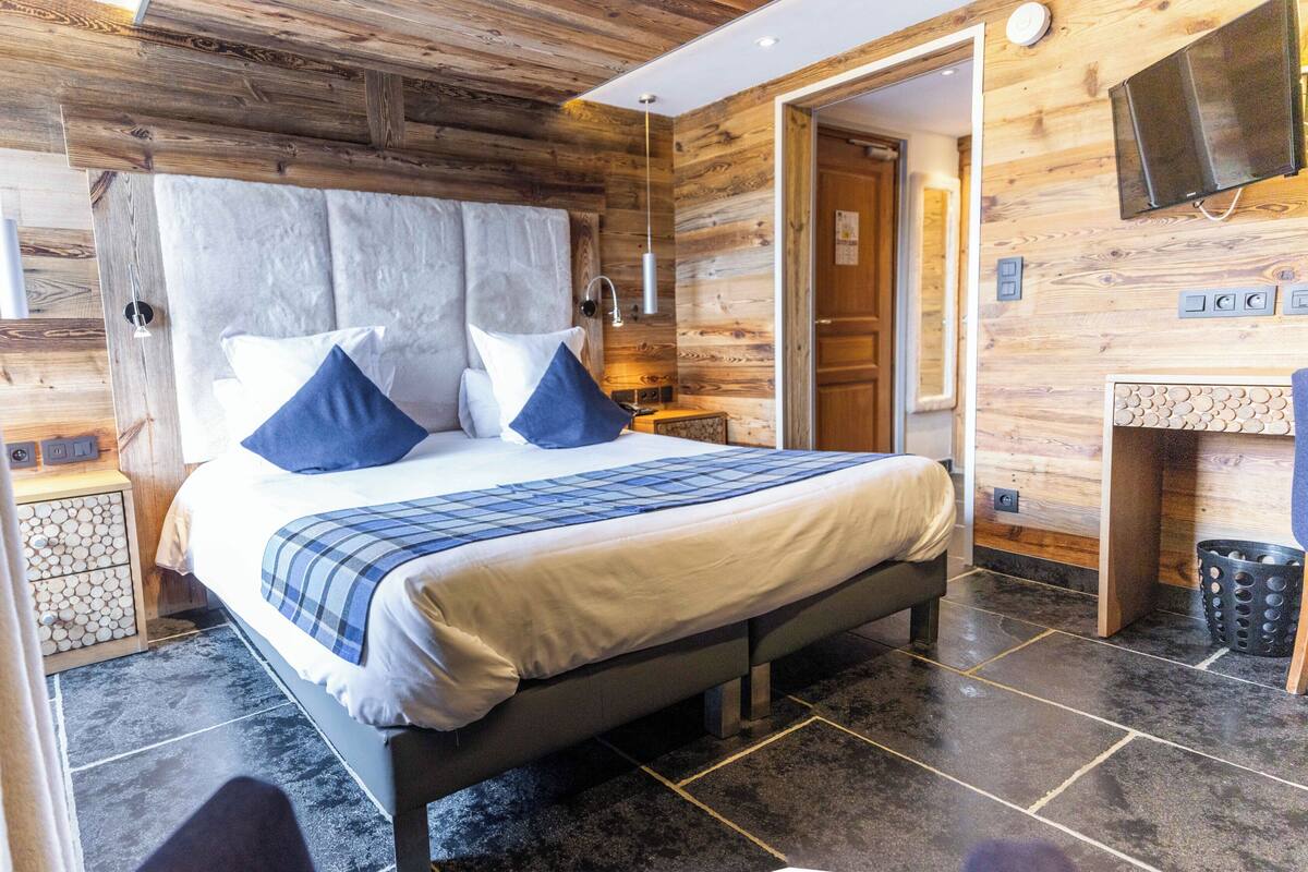 Ein modernes Schlafzimmer mit einem großen Bett, Holzwänden, Steinböden und einem kleinen Badezimmer mit Spiegel und Waschbecken.