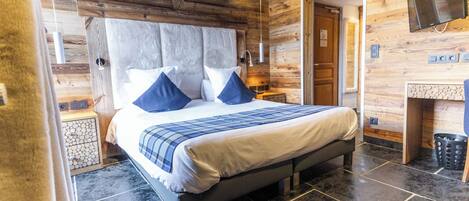 A modern bedroom with a large bed, wooden walls, a stone floor, and a small bathroom with a mirror and sink.