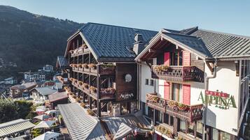 Un hotel con varios balcones decorados con flores, fachada de madera tradicional y vistas al pueblo y las montañas circundantes.