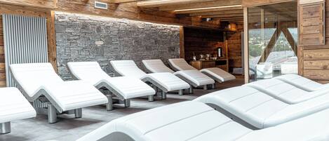 Un área de spa con paredes de madera, detalles de piedra y varias sillas de masaje blancas.