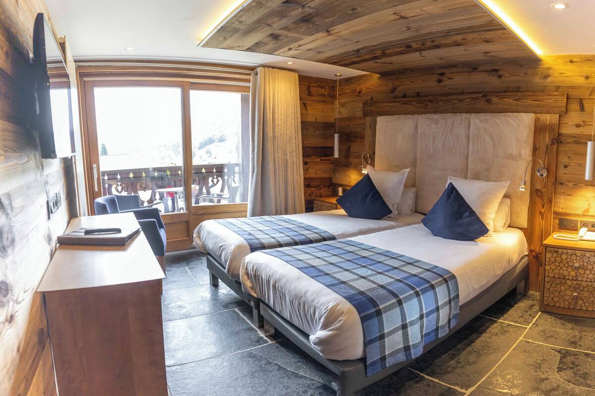 Ein holzgetäfeltes Zimmer im Chalet-Stil mit zwei Betten, einem Schreibtisch und einem großen Fenster.