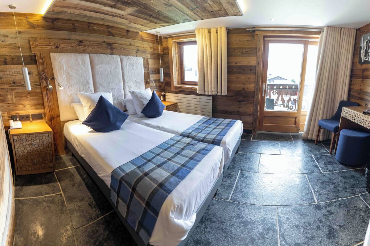 Ein Zimmer mit einem großen Bett, zwei Nachttischen, einem kleinen Schreibtisch und einem Fenster mit Vorhängen.