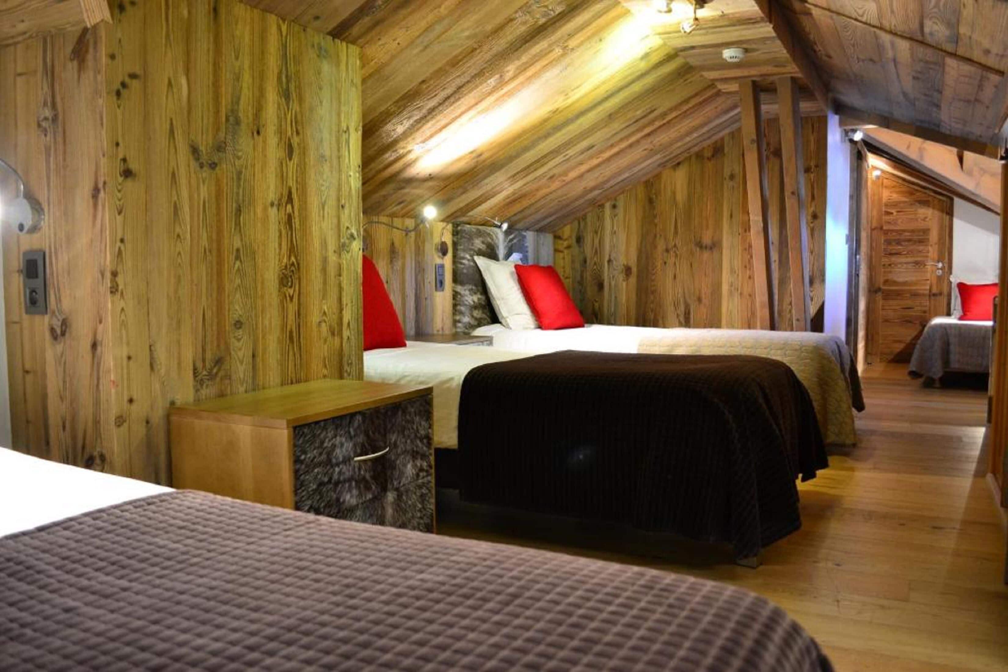 A wooden cabin with two beds, each with a red pillow, and a small wooden cabinet.