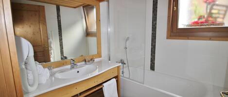 A bathroom with a wooden vanity, a large mirror, a white sink, a bathtub, and a window with a view of flowers.