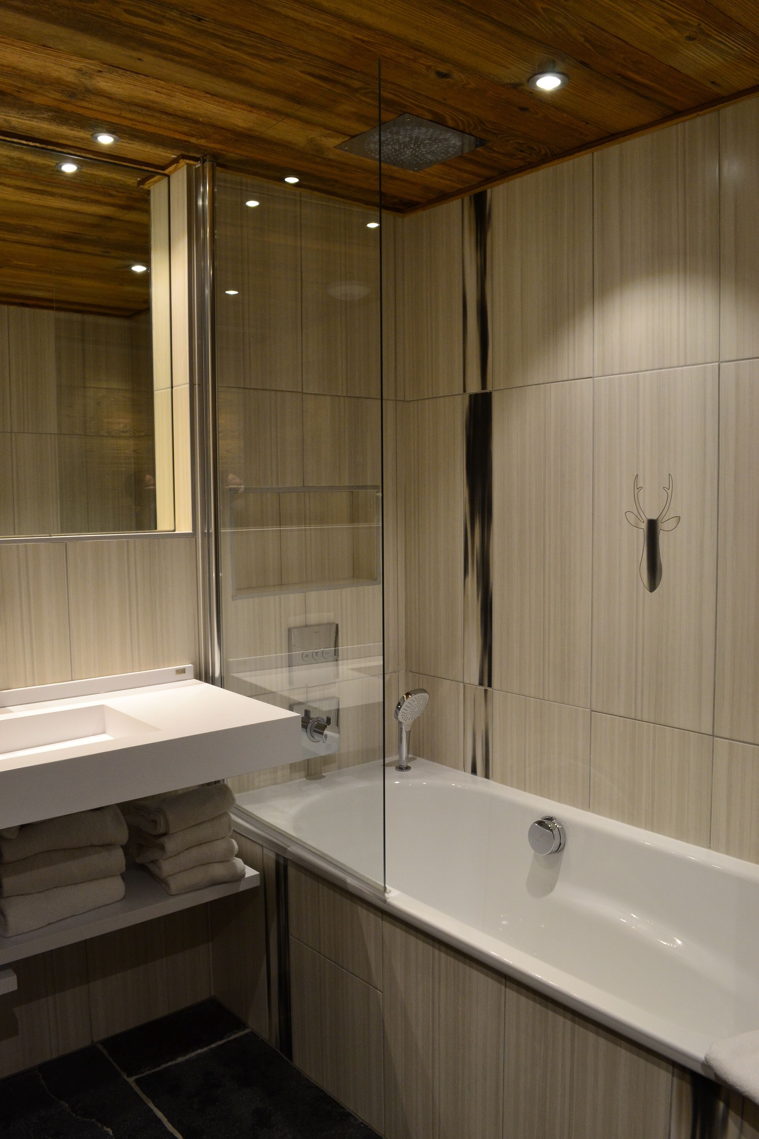 A modern bathroom with a wooden ceiling, a glass shower enclosure, a white bathtub, and a sink with a mirror.
