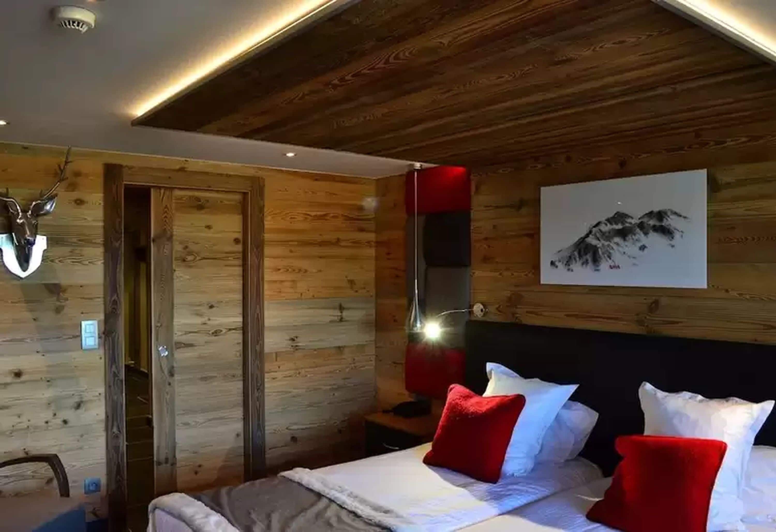 A wooden-paneled room with a bed, a red lamp, and a wall-mounted artwork.