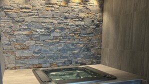 Un espace de détente avec un mur en pierre, un jacuzzi et un fauteuil.