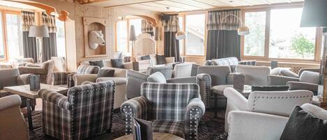 A cozy, well-lit lounge area with multiple seating options, including plaid and solid-colored armchairs, and a wooden coffee table.