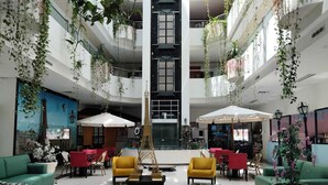 A spacious lobby with multiple seating areas, a central decorative structure, and hanging plants. - Paris FC HOTEL (Poza Rica)