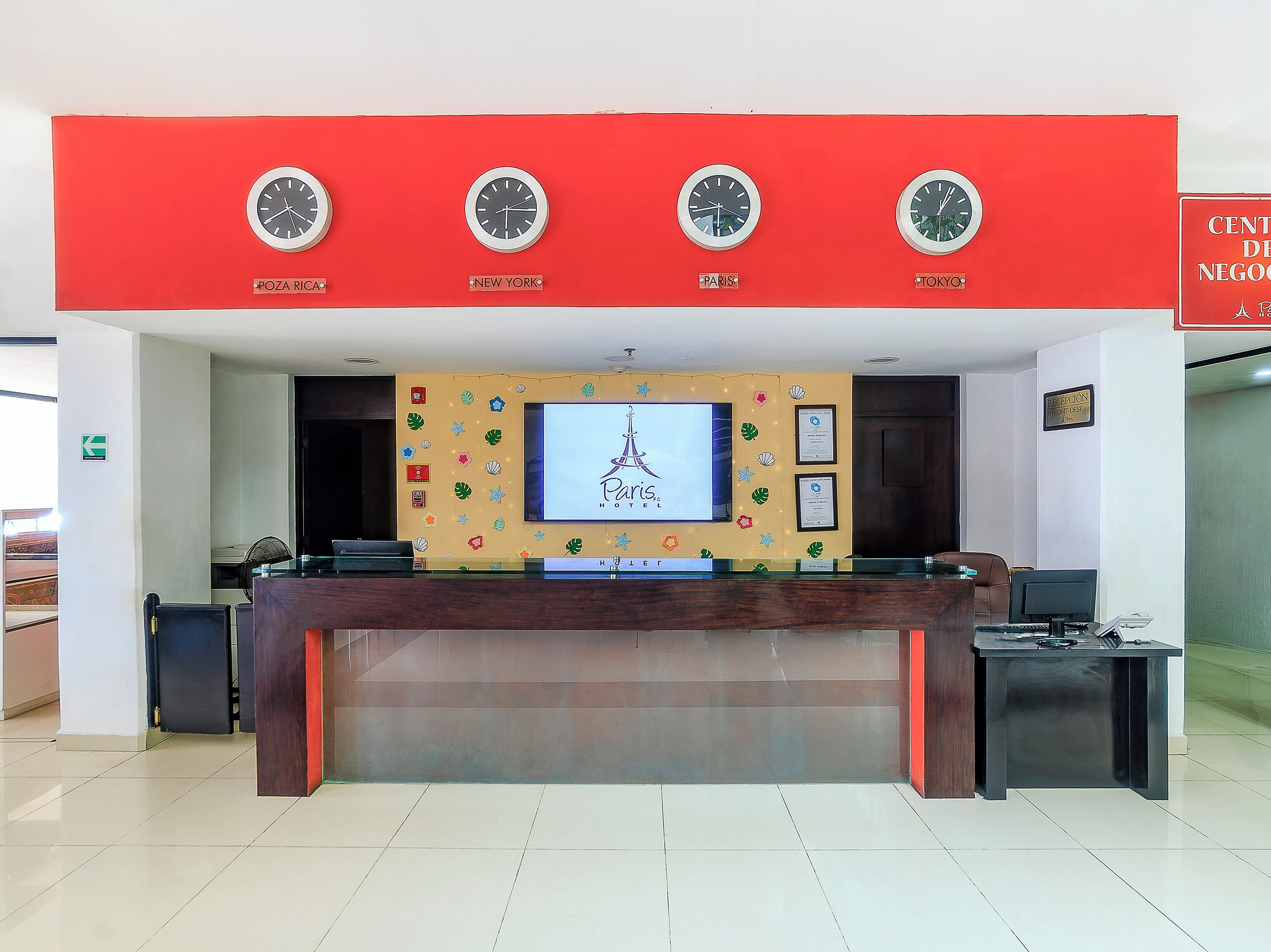 A hotel reception desk with clocks indicating different cities, a television screen with the Paris Hotel logo, and a reception desk area.