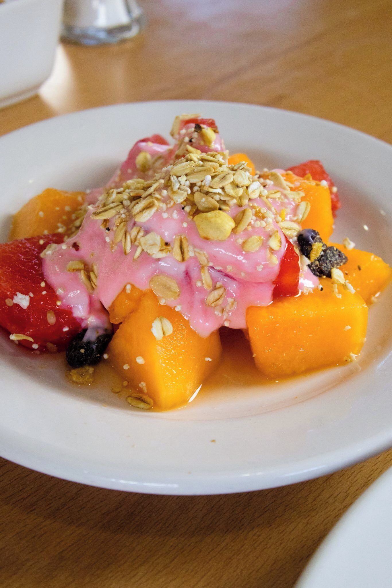 Una ensalada de frutas con diversas frutas y un topping rosado, posiblemente yogur o salsa, decorada con nueces.
