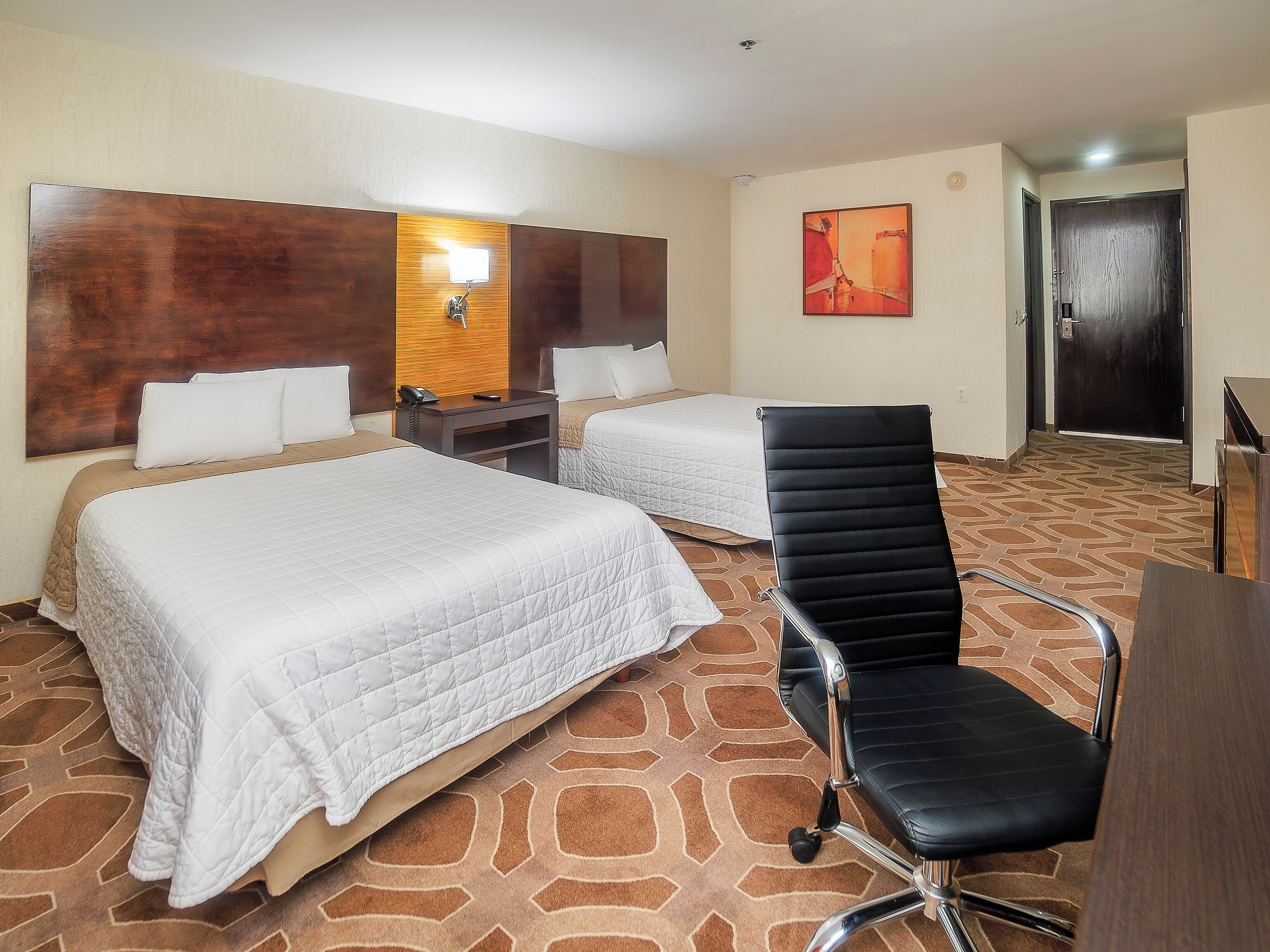 A hotel room with two beds, a desk, a chair, a telephone, and a painting on the wall.