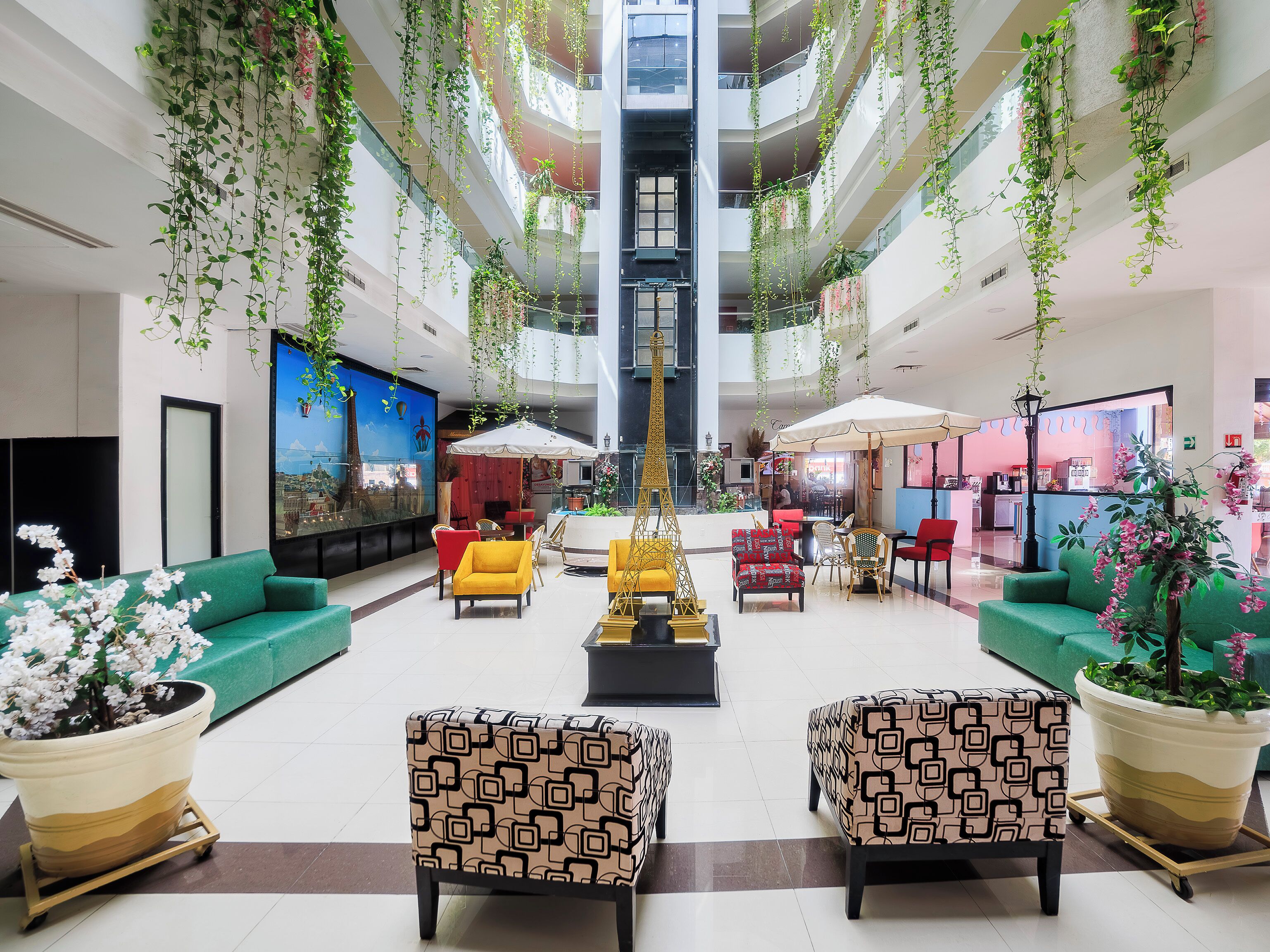 A spacious lobby with a central staircase, seating areas, and hanging plants.