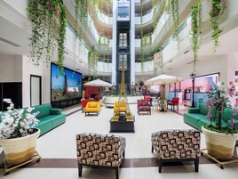 Un vestíbulo amplio con una escalera central, zonas de estar y plantas colgantes.