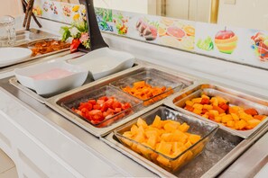 A buffet with various fruits and a white bowl.