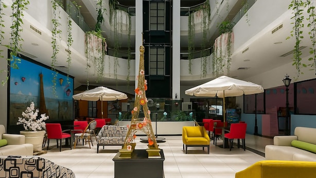 A modern indoor space with a central decorative structure, seating areas with red and yellow chairs, and hanging plants. - Paris FC HOTEL (Poza Rica)