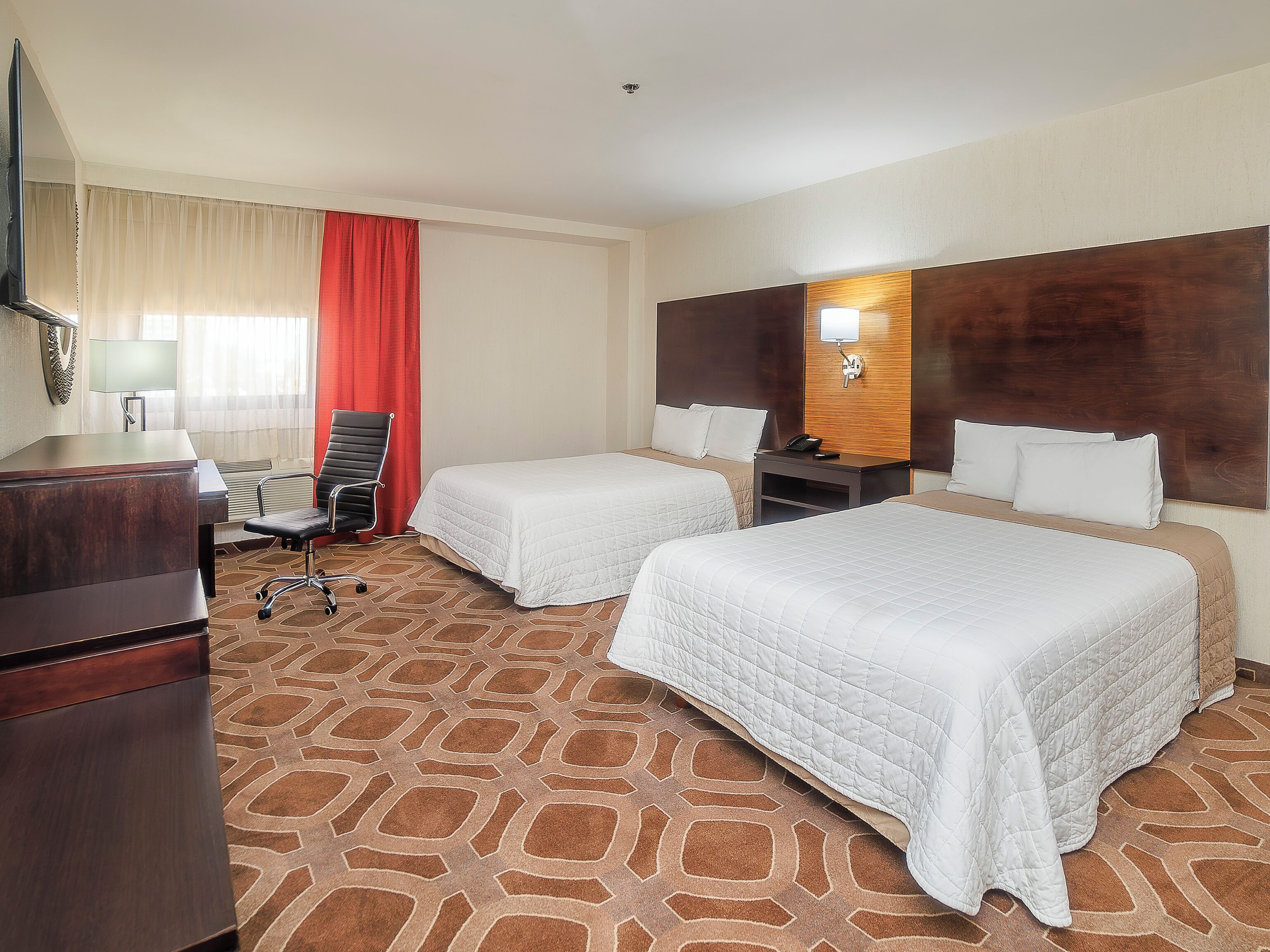 Une chambre d’hôtel avec deux lits, un bureau, une chaise et un téléviseur.