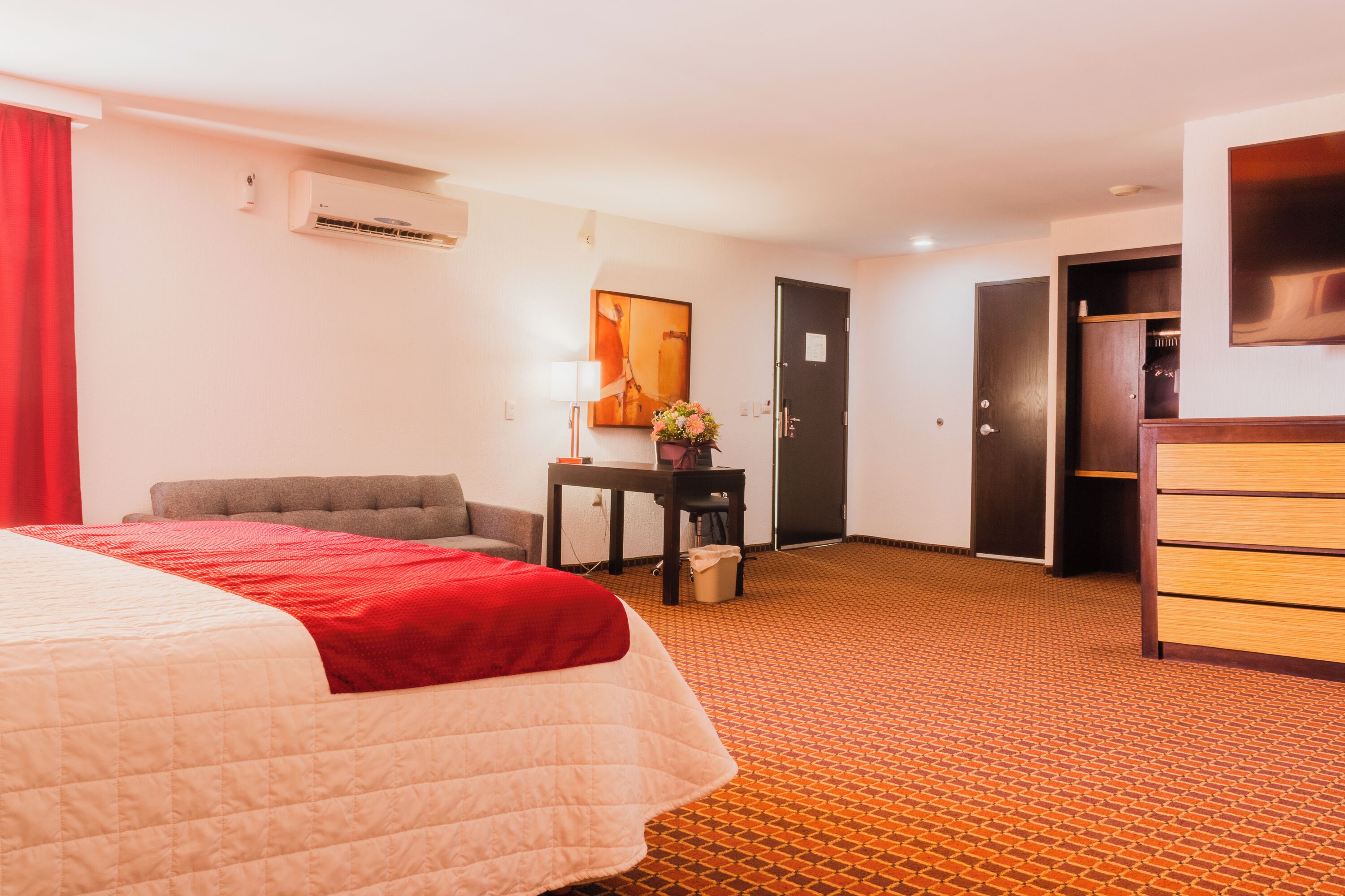 Habitación de hotel con cama, escritorio, silla, aire acondicionado, puerta y armario.