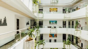 A multi-level atrium with glass railings, indoor plants, and artwork on the walls. - Paris FC HOTEL (Poza Rica)