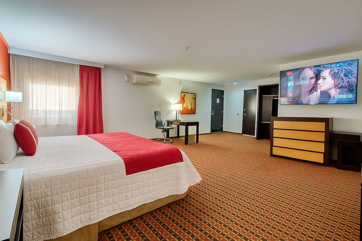 A hotel room with a bed, a desk, a chair, a TV, and a wardrobe.