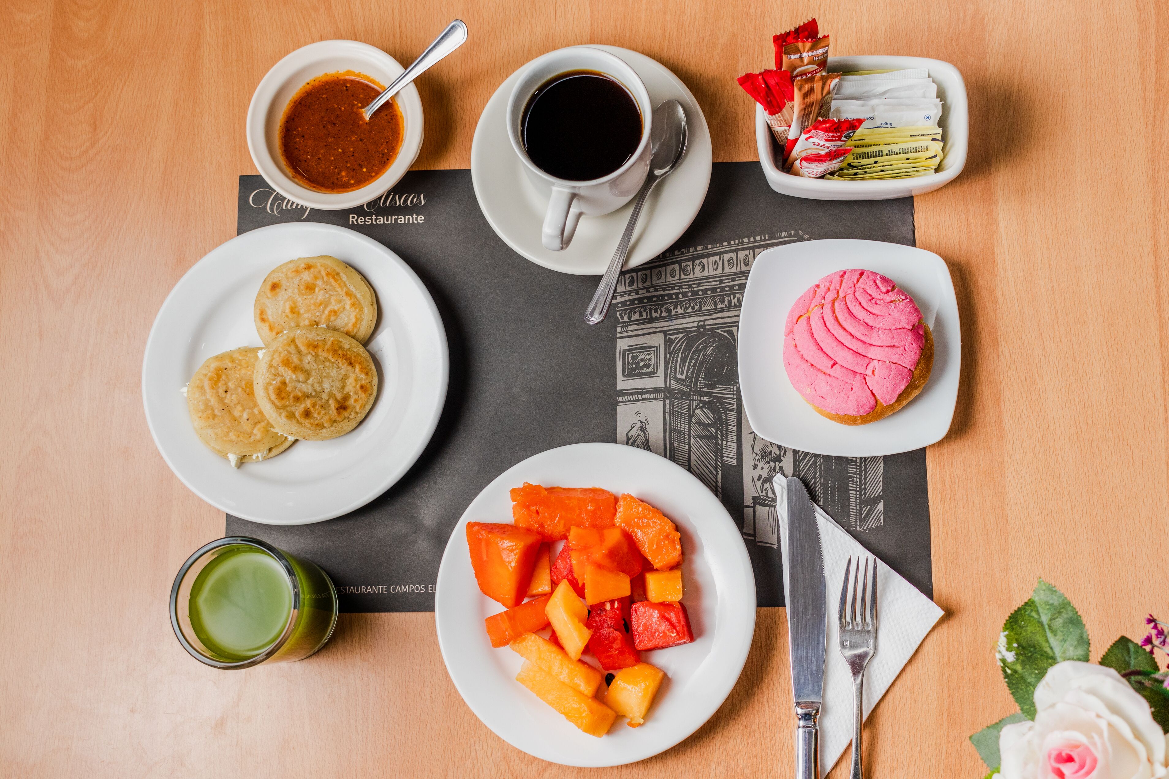 A table with breakfast items including pancakes, a pink dessert, fruit, and a cup of coffee.