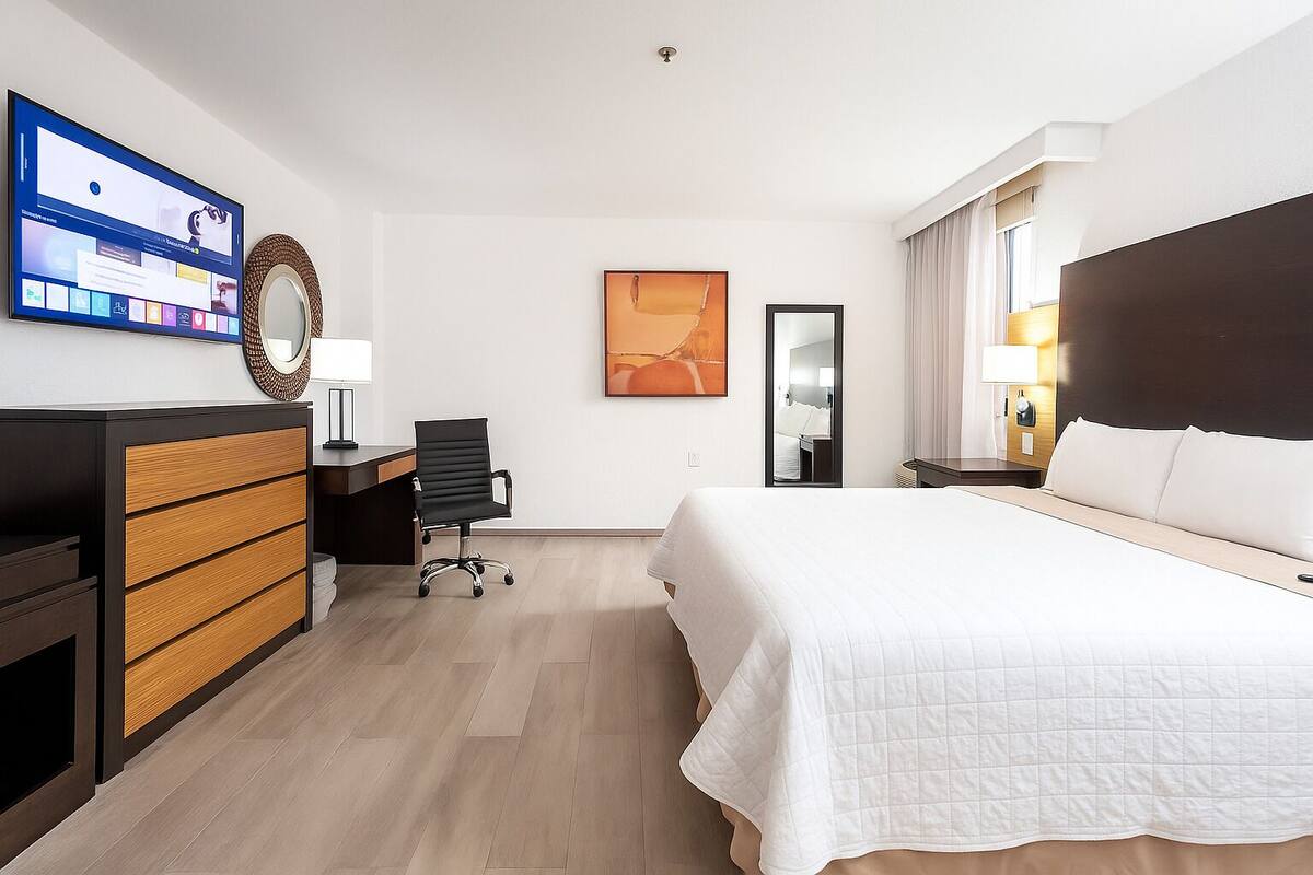 A hotel room with a bed, desk, chair, and a TV on the wall.