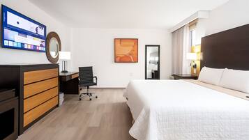 A hotel room with a bed, desk, chair, and a TV on the wall.