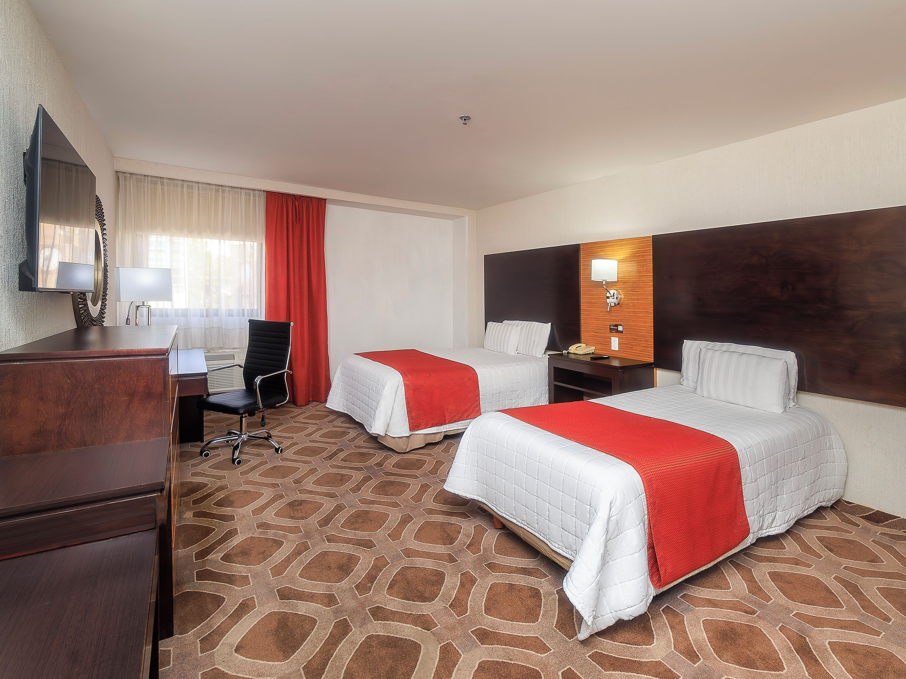 A hotel room with two beds, a desk, a chair, a TV, and a telephone.