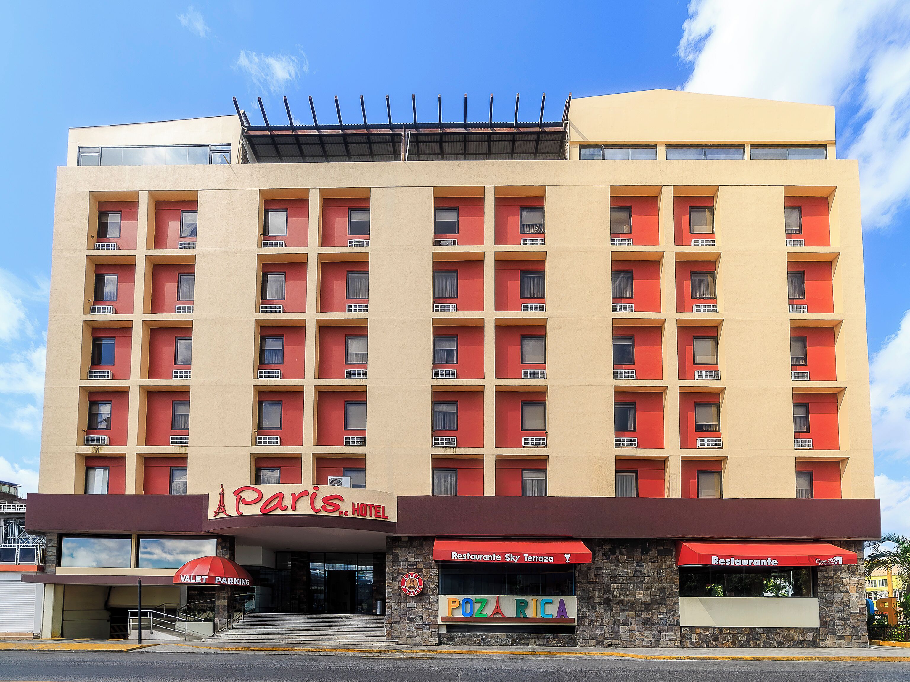 Un hotel de varios pisos con fachada roja y color beige, una entrada visible y señalización que indica 'Paris Hotel' y 'Restaurant Sky Terrace'.
