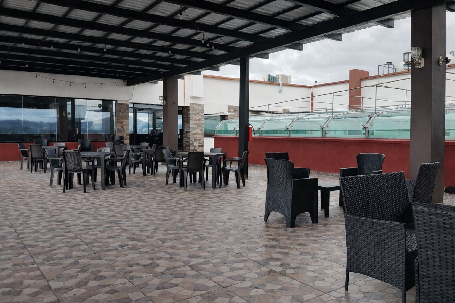 Area patio esterna con tavoli e sedie, tettoia e vista sulla città.