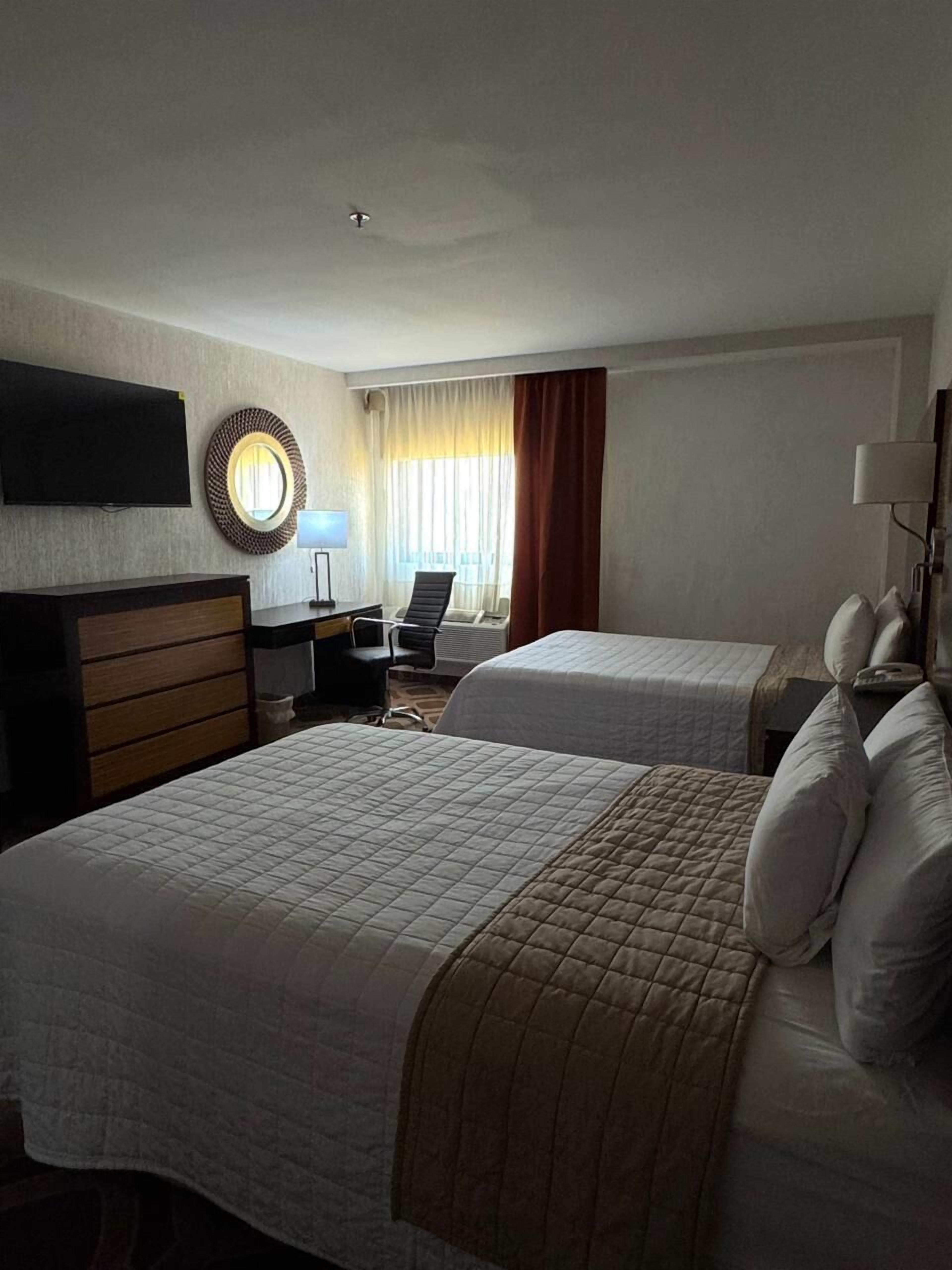 Una habitación de hotel con dos camas, un escritorio, una silla, un televisor y una ventana con cortinas.