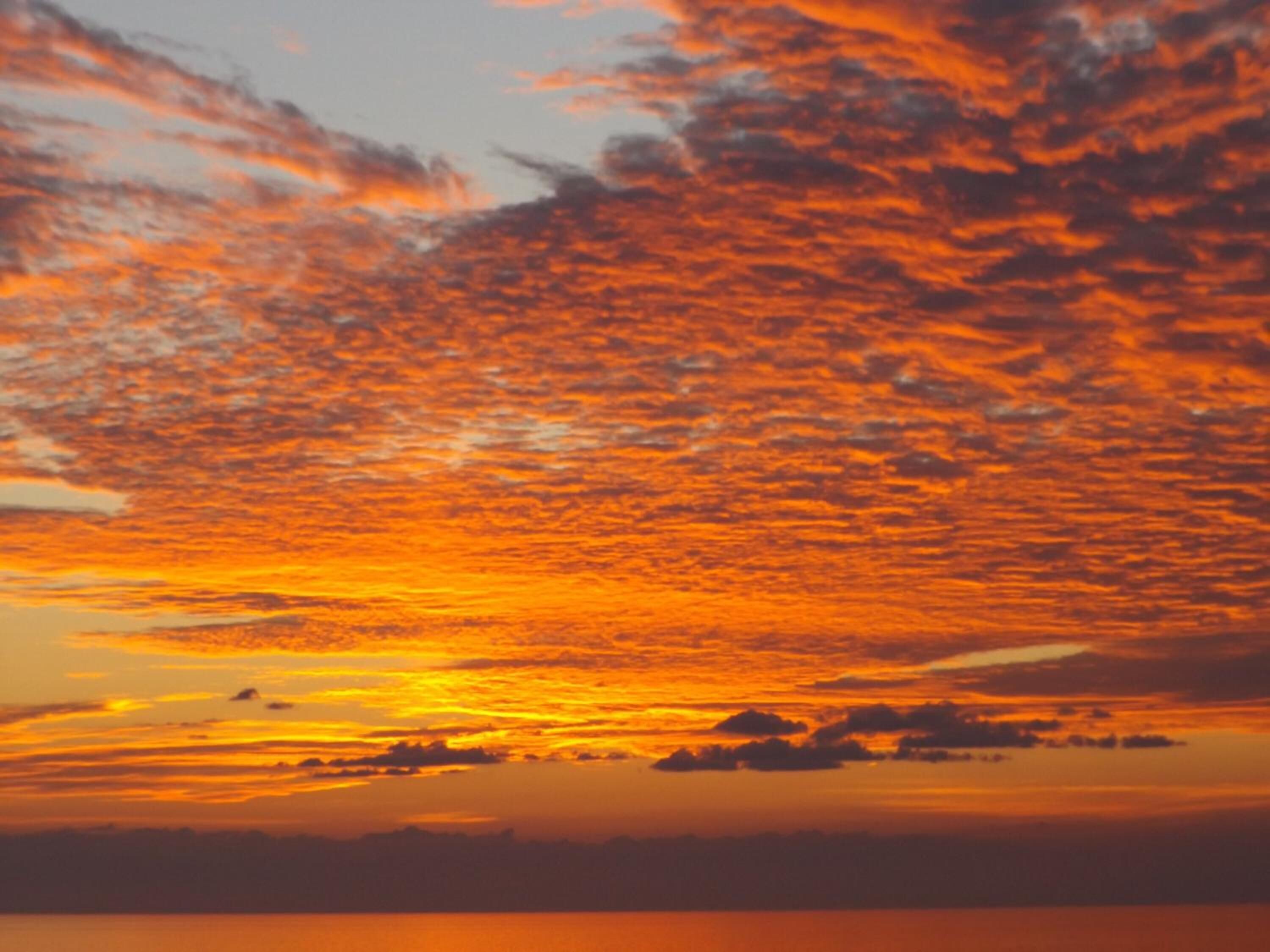 Ein Sonnenuntergang über ruhigem Gewässer mit einer fernen Küstenlinie.
