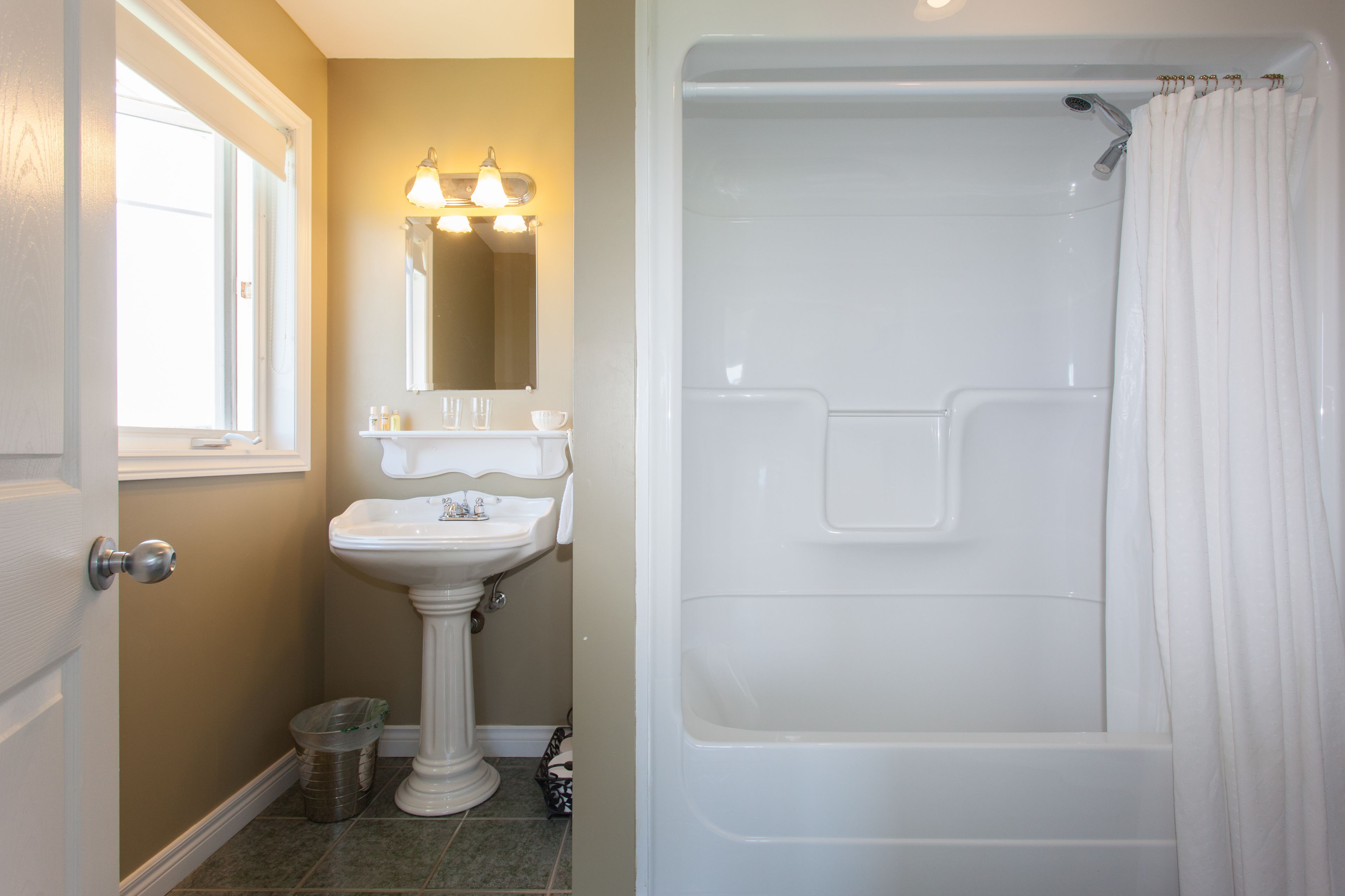 A bathroom with a pedestal sink, a bathtub, and a shower curtain.