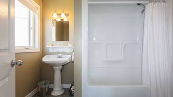 A bathroom with a pedestal sink, a bathtub, and a shower curtain.
